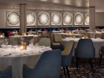 Ein elegantes Restaurant auf dem Kreuzfahrtschiff Celebrity Ascent, mit zahlreichen runden, festlich gedeckten Tischen, blauen Stühlen und großer Wandkunst.