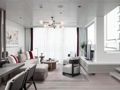 Moderner Wohnbereich auf der Celebrity Ascent. Helles Sofa, Tische, Sessel, Kronleuchter, große Fenster und eine Treppe sind zu sehen.