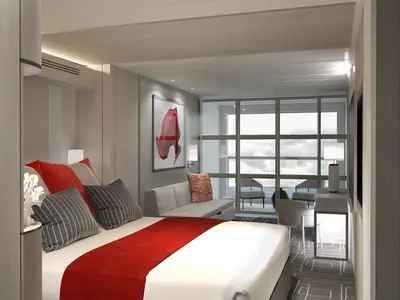 Helle, modern eingerichtete Kabine auf der Celebrity Beyond mit Doppelbett, roten Akzenten und Sofa. Große Fensterfront führt zu einem Balkon mit Meerblick und Sitzgelegenheiten.