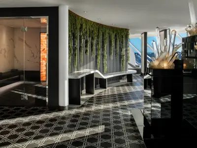 Ein luxuriöses Spa-Interieur mit einer großen vertikalen Pflanzenwand. Rechts stehen beleuchtete Kristallskulpturen, links ist der Eingang zu einer Dampfsauna mit Marmorwänden und einer Himalaya-Salzziegelwand zu sehen. Der Boden ist mit einem schwarzen-weißen Muster gefliest.