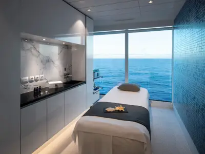 Ein heller Spa-Raum auf der Celebrity Beyond mit Behandlungsbett, Arbeitsplatte aus Marmor und einem großen Fenster mit Panoramablick auf das weite, blaue Meer.