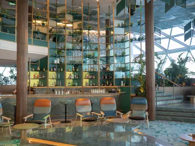 Elegante Bar mit grünem Marmortresen, beleuchteten Regalen, Pflanzen und modernen Lounge-Sesseln.