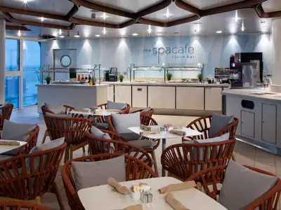 Moderne Spa Café und Juice Bar der Celebrity Edge mit Buffet, Tischen und Sesseln. Große Fenster bieten Tageslicht und Ausblick.