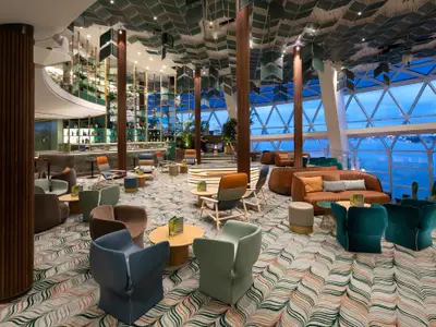 Eine moderne Bar und Lounge mit verschiedenen Sitzbereichen, einer gut bestückten Bar und großen Fenstern, die einen weiten Blick auf das Meer und den Horizont bieten. Die Decke ist mit dekorativen Elementen versehen.
