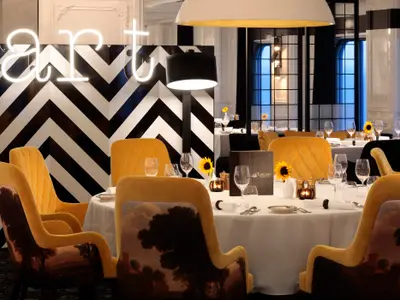 Stilvolles Restaurant mit gelben Samtstühlen, schwarz-weißem Chevron-Muster und gedeckten Tischen.