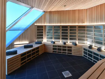 Heller Saunaraum auf der Celebrity Edge mit Holzverkleidung, Bänken und Handtüchern. Große Fenster mit Meerblick und Infrarotwand.