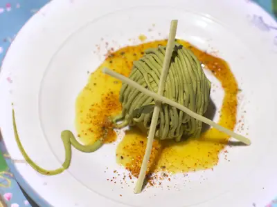 Kunstvoll angerichtetes Dessert mit grüner Creme und gelber Sauce auf weißem Teller.