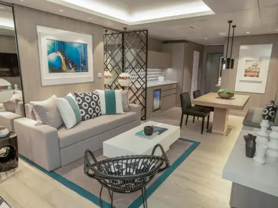 Moderne Suite der Celebrity Edge mit hellem Wohn- und Essbereich. Graues Sofa, weißer Couchtisch, Holztisch mit Stühlen, Sitzbank und eine Pantryküche sind sichtbar.