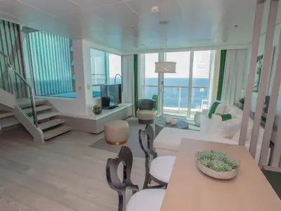 Moderne, zweistöckige Kreuzfahrtsuite mit großen Fenstern mit Meerblick. Helle Einrichtung mit weißen Möbeln und grünen Akzenten.