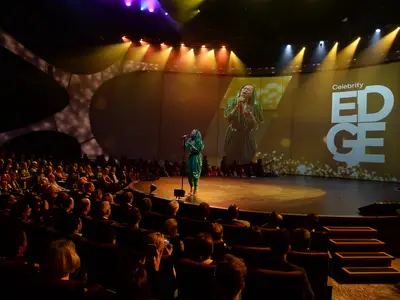 Sängerin tritt auf der Bühne eines Theaters mit großem Bildschirm und Publikum an Bord der Celebrity Edge auf.