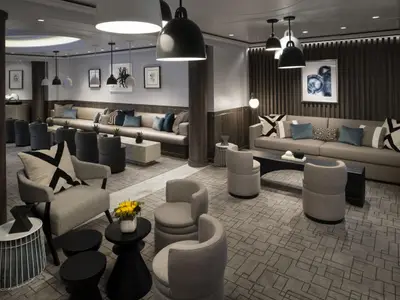Eine moderne und elegante Lounge mit verschiedenen Sitzbereichen, darunter Sofas, Sessel und kleine Tische. Die Einrichtung ist in Grautönen mit blauen Akzenten gehalten. Dunkle Holzvertäfelungen und Kunstwerke schmücken die Wände. Verschiedene Hängelampen spenden gedämpftes Licht.