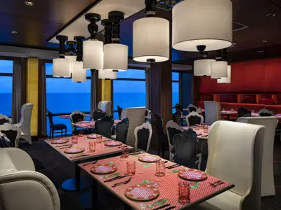 Blick in ein stilvolles Restaurant der Celebrity Equinox mit Tischen am Fenster zum Meer, roten Sitzbänken und eleganten Hängelampen.