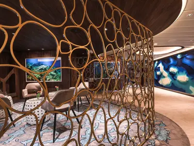 Moderne Lounge mit goldenem Raumteiler, bequemen Sitzen, Unterwasser-Kunst und blauer Wandgestaltung.
