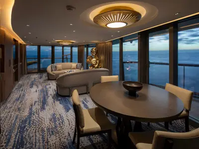 Eine geräumige Lounge auf der Celebrity Flora mit Meerblick durch große Fenster. Ess- und Wohnbereiche mit stilvollen Möbeln und Teppich sind zu sehen.