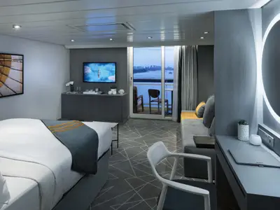 Moderne Kabine auf der Celebrity Millennium mit Bett, Sofa, Schreibtisch und Balkon. Blick auf das Meer. Helle Einrichtung in Grau.
