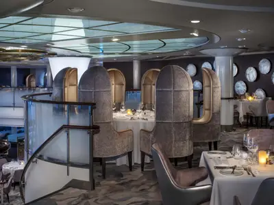 Blick in ein elegantes Restaurant auf der Celebrity Millennium. Gedeckte Tische, hohe Stühle, Glas-Treppe, modernes Design.