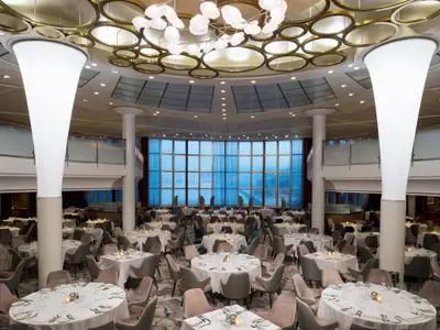 Elegantes Restaurant auf der Celebrity Millennium mit vielen eingedeckten Tischen, stilvollen Stühlen und großen Panoramafenstern. Moderne Deckenbeleuchtung und leuchtende Säulen prägen den Raum.
