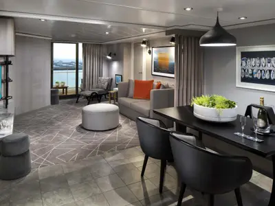 Die elegante Suite der Celebrity Summit zeigt einen Wohnbereich mit Sofa und Sessel, einen Essbereich mit Champagner und Pflanzen. Große Fenster geben Meerblick frei.