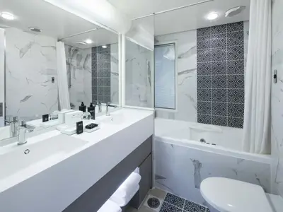 Ein modernes Badezimmer mit zwei Waschbecken, einem großen Spiegel, einer Badewanne und einer Duschkabine. Die Wände sind mit weißen Marmorfliesen und einem dunklen, gemusterten Akzentbereich versehen.