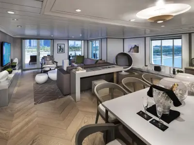 Luxuriöse Suite auf der Celebrity Summit. Heller Wohn- und Essbereich mit modernen Möbeln und Parkettboden. Große Fenster bieten Meerblick, Balkonzugang. Eine gekühlte Champagnerflasche steht bereit.