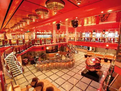 Das rote Atrium "Delle Delizie" an Bord der Costa Deliziosa mit einer Bar, eleganten Treppen und einer großen, runden Kunstskulptur im Zentrum.