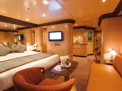 Blick in eine geräumige, elegante Suite an Bord der Costa Deliziosa mit einem großen Bett, einer Sitzecke und Champagner auf dem Tisch.