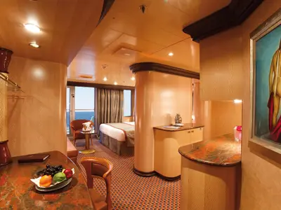 Elegante Suite an Bord der Costa Deliziosa mit Doppelbett, Sitzbereich, Balkonzugang mit Meerblick und einem großen Gemälde an der Wand.