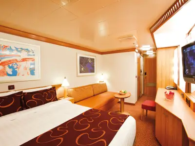 Eine gemütlich eingerichtete Balkonkabine an Bord der Costa Deliziosa mit großem Doppelbett, orangefarbenem Sofa und Fernseher.