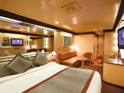 Blick in eine gemütliche Mini-Suite an Bord der Costa Deliziosa mit großem Doppelbett, Sitzecke und Fernseher.