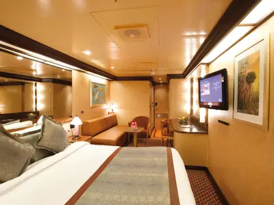 Blick in eine gemütliche Mini-Suite an Bord der Costa Deliziosa mit einem großen Bett, Sofa, Couchtisch und TV an der Wand.