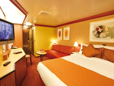 Balkonkabine an Bord der Costa Deliziosa mit Doppelbett, rotem Sofa, Fernseher und Wandbildern in warmen Farben.