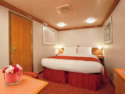 Gemütliche Innenkabine an Bord der Costa Deliziosa mit einem großen Doppelbett, Nachttischlampen und rötlicher Dekoration.