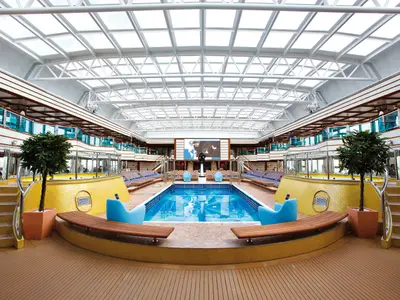 Symmetrische Ansicht des überdachten Pools "Azzurro Blu" an Bord der Costa Deliziosa mit gelben Mosaikwänden und einem großen Glasdach.