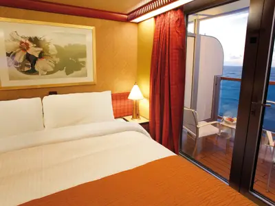 Eine gemütliche Balkonkabine an Bord der Costa Deliziosa mit einem Doppelbett, warmem Licht und Blick auf den Balkon und das weite blaue Meer.