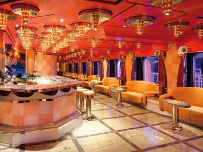 Innenansicht der stilvollen Vanilla Bar an Bord der Costa Deliziosa mit orangefarbenen Ledersofas und auffälligen Deckenleuchten.