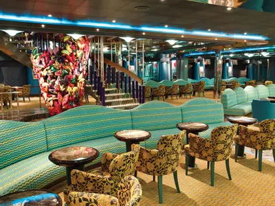 Die farbenfroh gestaltete Grand Bar Mirabilis an Bord der Costa Deliziosa mit gemusterten Sesseln.