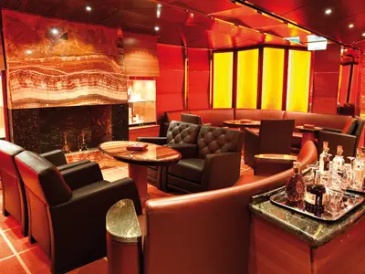 Elegante Bar-Lounge an Bord der Costa Deliziosa. Rotes Interieur, Onyx-Kamin, bequeme Ledersessel und Serviertabletts mit Spirituosen schaffen eine luxuriöse Atmosphäre.