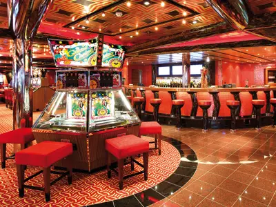 Das beleuchtete Gaius Casino an Bord der Costa Deliziosa zeigt Spielautomaten, eine runde Bar mit roten Hockern und roten Fliesenwänden.