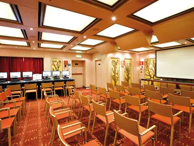 Der Konferenzraum Kipros an Bord der Costa Deliziosa zeigt Stuhlreihen vor einer großen Leinwand und Computerbildschirmen.
