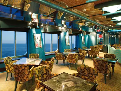 Ein eleganter Salon der Costa Deliziosa mit Meerblick. Mehrere Tische, floral gemusterte Sessel, blaue Wände und eine reflektierende Decke kennzeichnen den Raum.