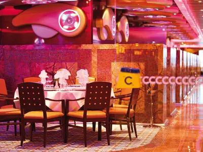 Blick in das elegant beleuchtete Restaurant Albatros an Bord der Costa Deliziosa, mit festlich gedeckten Tischen und orangen Stühlen. Die Wände sind mit roten Mosaikfliesen und Marmor verziert. Eine leuchtende Deckeninstallation sorgt für eine warme Abendstimmung.