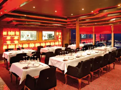 Eingedeckte Tische im stilvollen Club-Restaurant Deliziosa an Bord der Costa Deliziosa mit Blick auf die Küche.