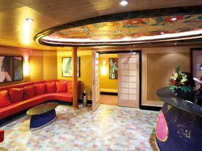 Die Rezeption des Samsara Spa an Bord der Costa Deliziosa mit einem roten Ledersofa, bunter Deckenbemalung und einer Mitarbeiterin.