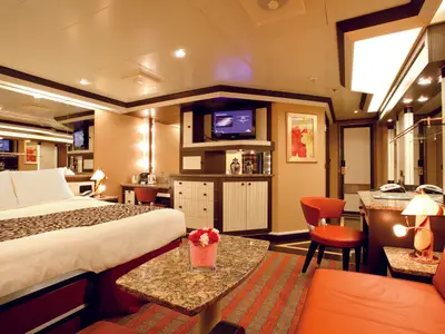 Eine geräumige und elegante Suite an Bord der Costa Deliziosa. Sie zeigt ein Doppelbett, eine Sitzecke und einen Medienbereich.