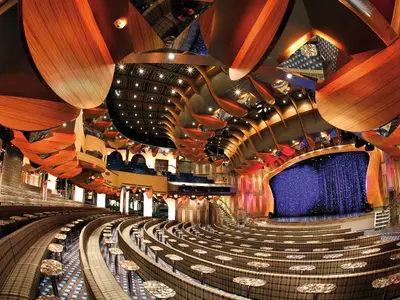 Weitwinkel-Ansicht des Duse-Theaters an Bord der Costa Deliziosa mit geschwungener Deckenkonstruktion aus Holz und einer blauen Bühne.