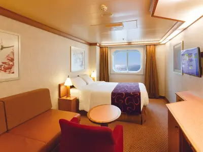 Helle Aussenkabine an Bord der Costa Diadema mit beigem Interieur. Sie zeigt ein Doppelbett, ein braunes Sofa, einen roten Sessel und ein Fenster mit Meerblick.