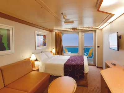 Blick in eine moderne Balkonkabine an Bord der Costa Diadema mit Doppelbett, orangefarbenem Sofa und privatem Balkon mit Meerblick.