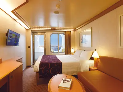 Balkonkabine an Bord der Costa Diadema. Zu sehen sind ein Doppelbett, ein Ledersofa, Schreibtisch, TV und ein Balkonzugang mit weitem Meerblick.