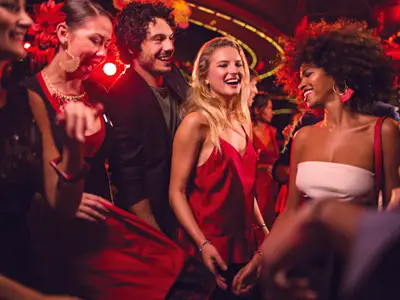 A diverse group of smiling people dancing and having fun at a lively, red-lit club or lounge on the Costa Diadema cruise ship.