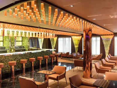 Eine elegant beleuchtete Bar-Lounge an Bord der Costa Diadema mit zahlreichen Deckenlichtern, einer grünen Mosaik-Bar und bequemen braunen Ledersesseln.